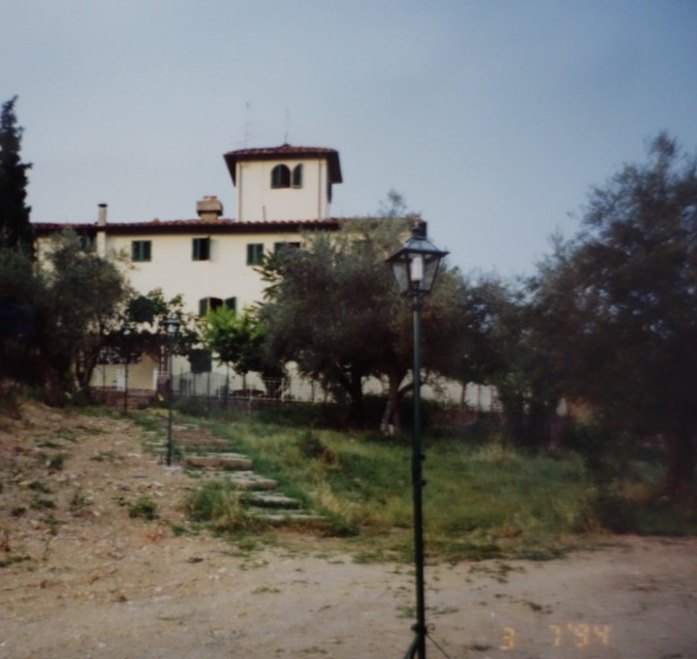 The villa seen from below the hill in 1994, with a stone path, a lamp post, and olive trees.
