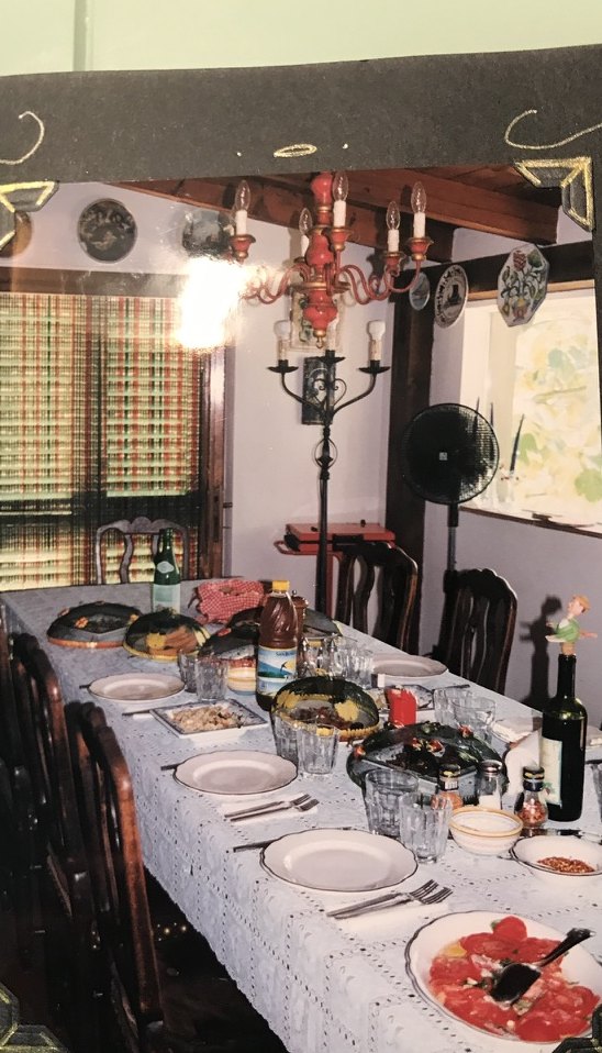 A long indoor dining table laid with a white cloth, plates, and glasses, under a candelabra.