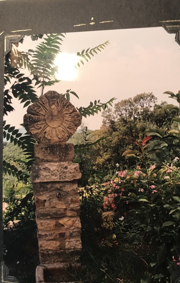 A carved stone fountain among garden plants and roses.