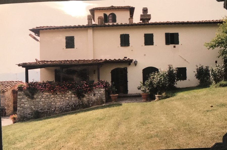 The cream stucco facade of Villa Giaggioli, with green shutters, a flowered loggia, and the colombaia on the roof.