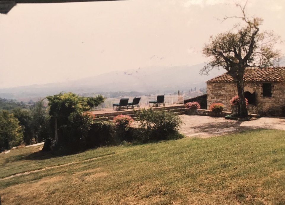 Chaise longues on a terrace beside a stone building, looking over hazy hills.